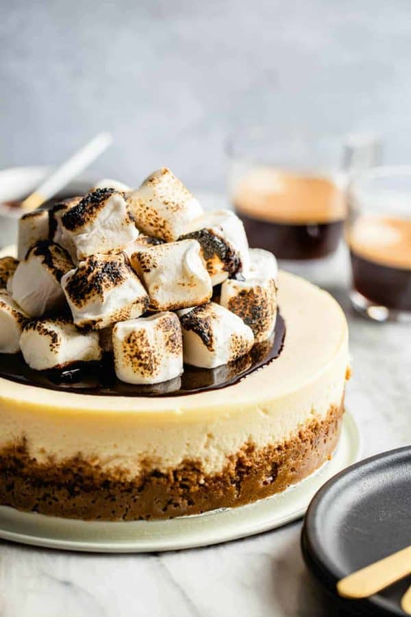 S'mores cheesecake topped with toasted marshmallows in front of cups of espresso