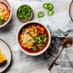 White bean chili in bowls on a countertop next to cornbread and sliced jalapenos