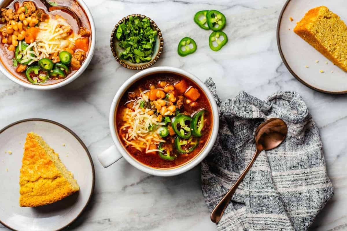 White bean chili in bowls on a countertop next to cornbread and sliced jalapenos