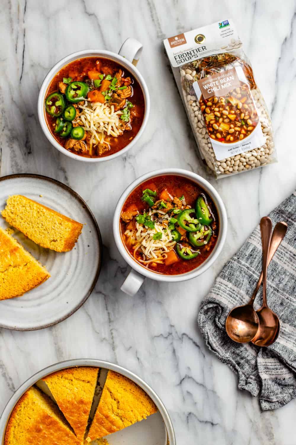 Bowls of white bean chicken chili next to plates of cornbread