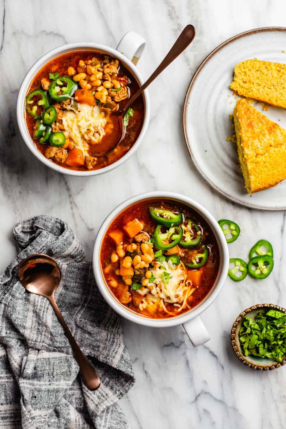 Two white bowls filled with chicken chili next to a plate of cornbread