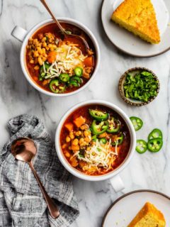 Two bowls of white bean chicken chili topped with cheese and sliced jalapeno peppers