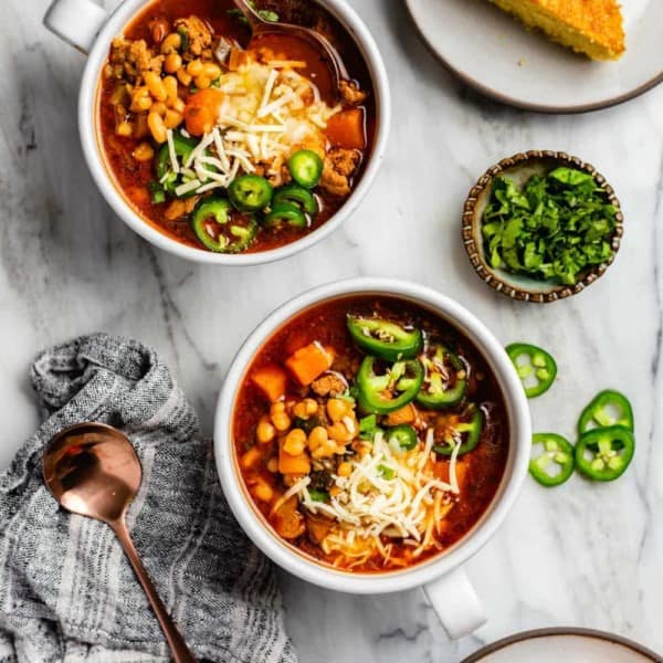 Two bowls of white bean chicken chili topped with cheese and sliced jalapeno peppers