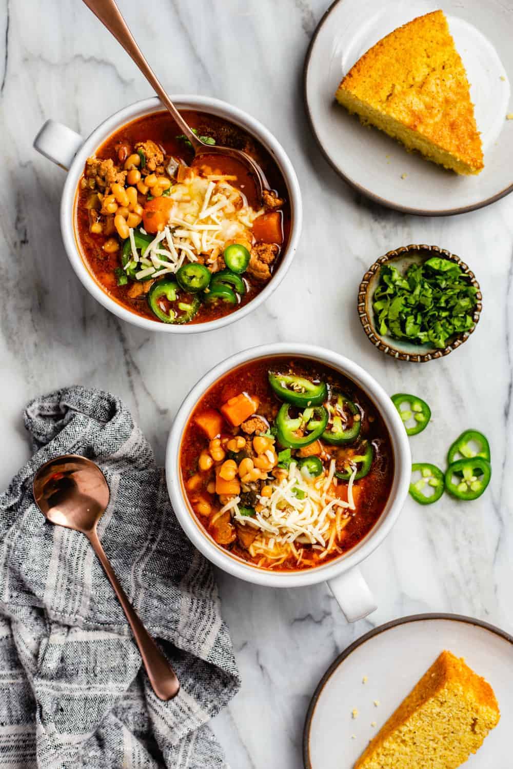 Two bowls of white bean chicken chili topped with cheese and sliced jalapeno peppers