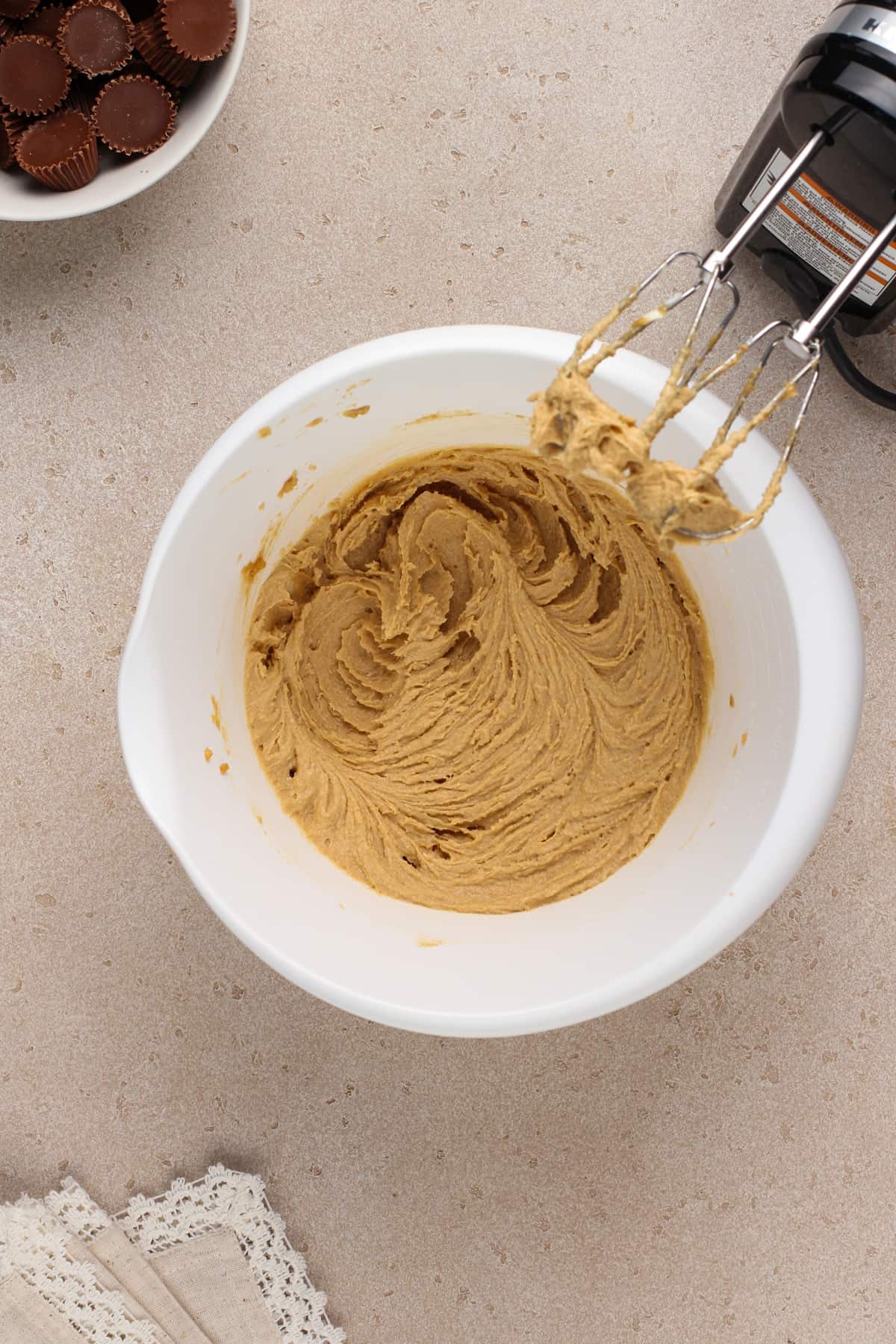 Butter, sugar, and peanut butter creamed together in a white mixing bowl.