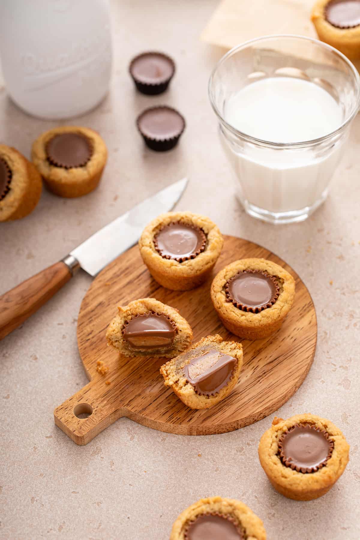 Three peanut butter cup cookies arranged on a wooden board. One of the cookies has been cut in half.