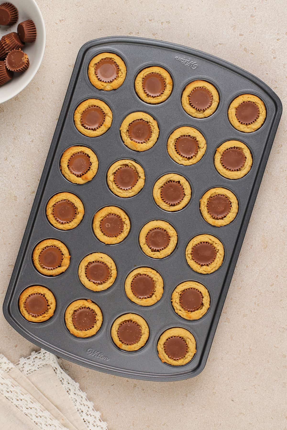 Peanut butter cups pressed into baked peanut butter cookies in a mini muffin tin.