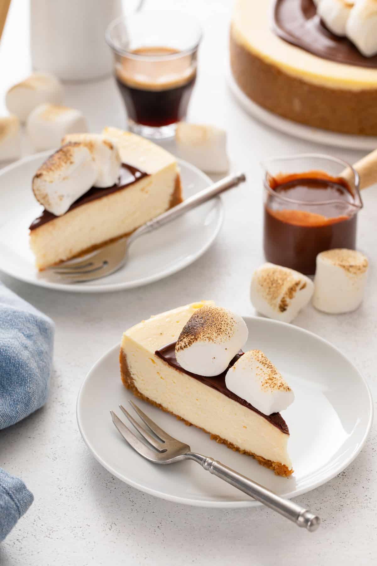 Two slices of s'mores cheesecake, each next to a fork on a white plate.