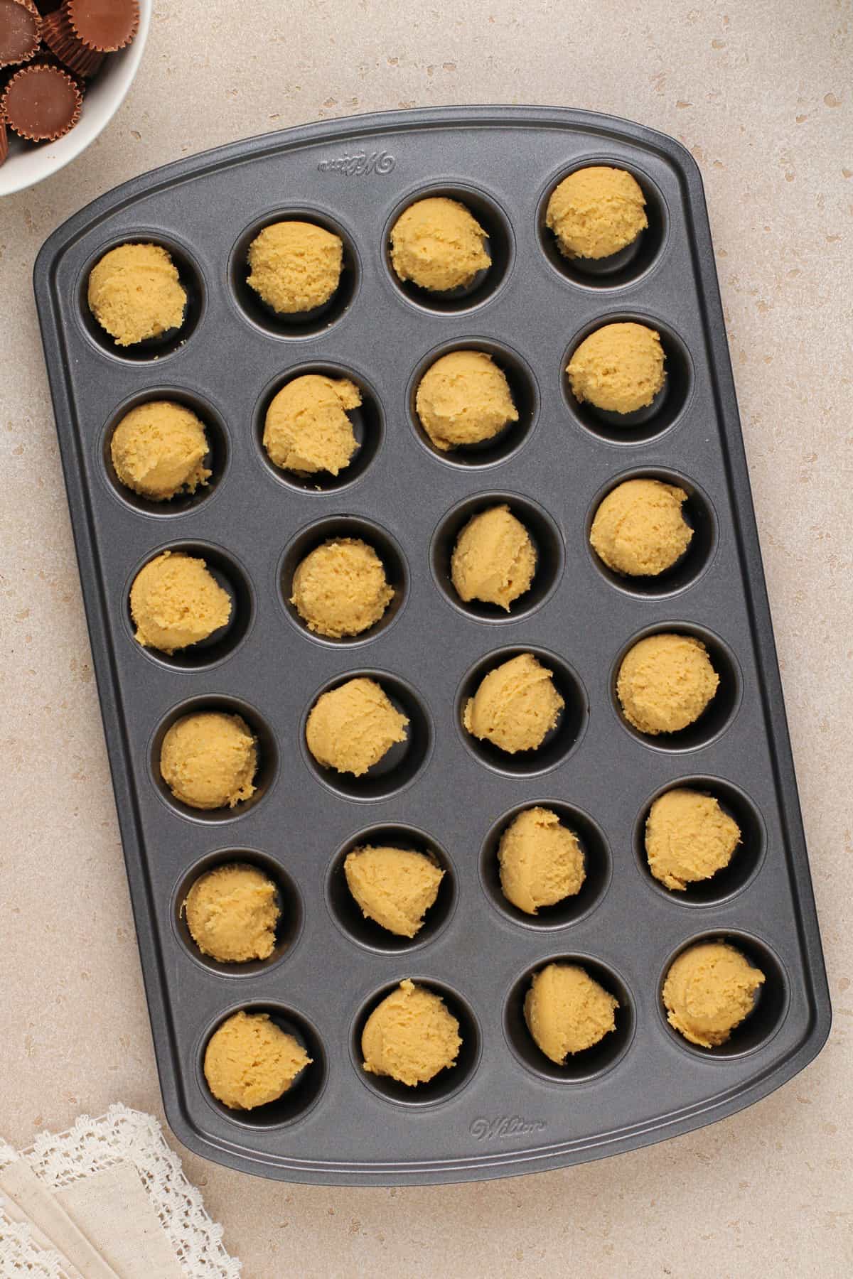 Peanut butter cookie dough portioned into a mini muffin tin.