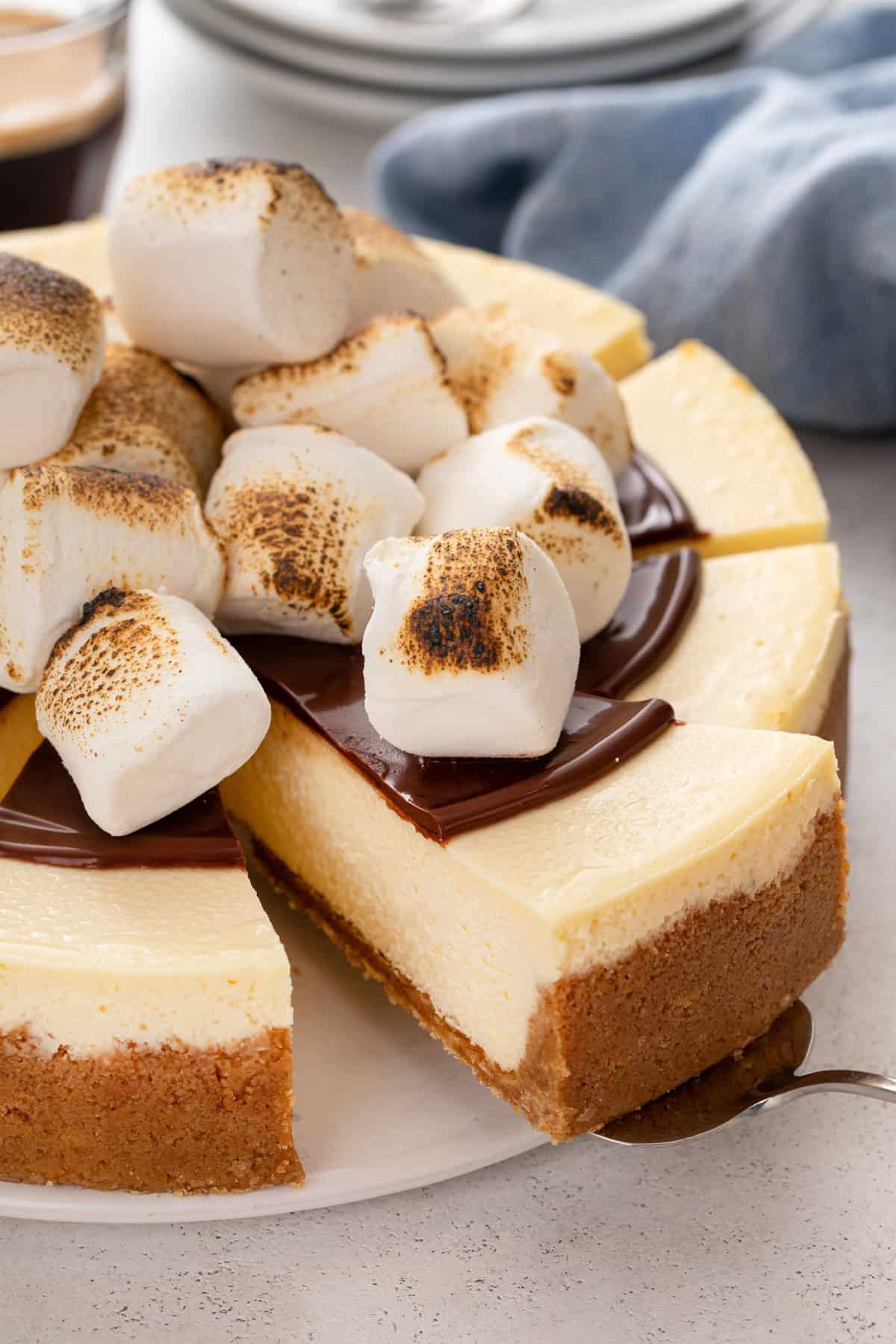 Cake server lifting a slice of s'mores cheesecake from a cake plate.