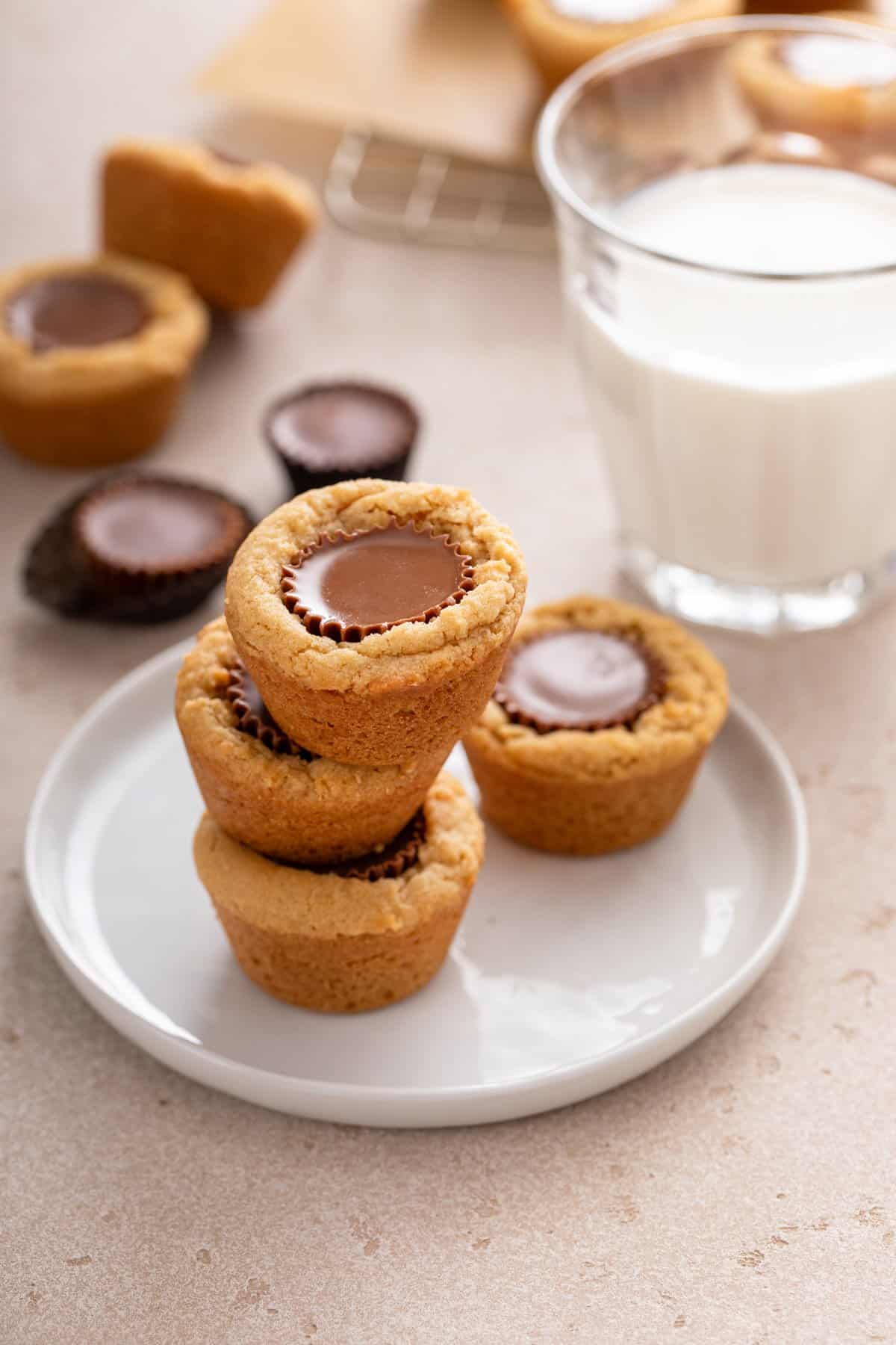 Three peanut butter cup cookies stacked on a white plate in front of a glass of milk.