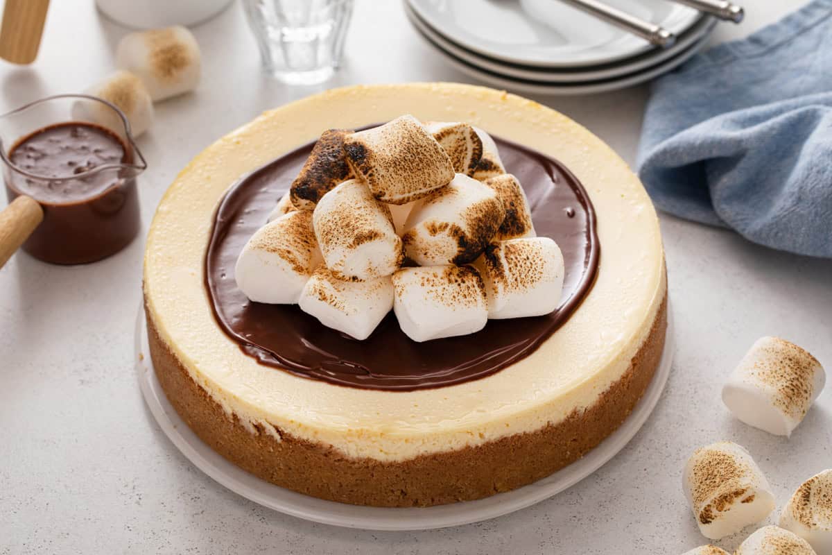 Whole s'mores cheesecake garnished with hot fudge sauce and toasted marshmallows.