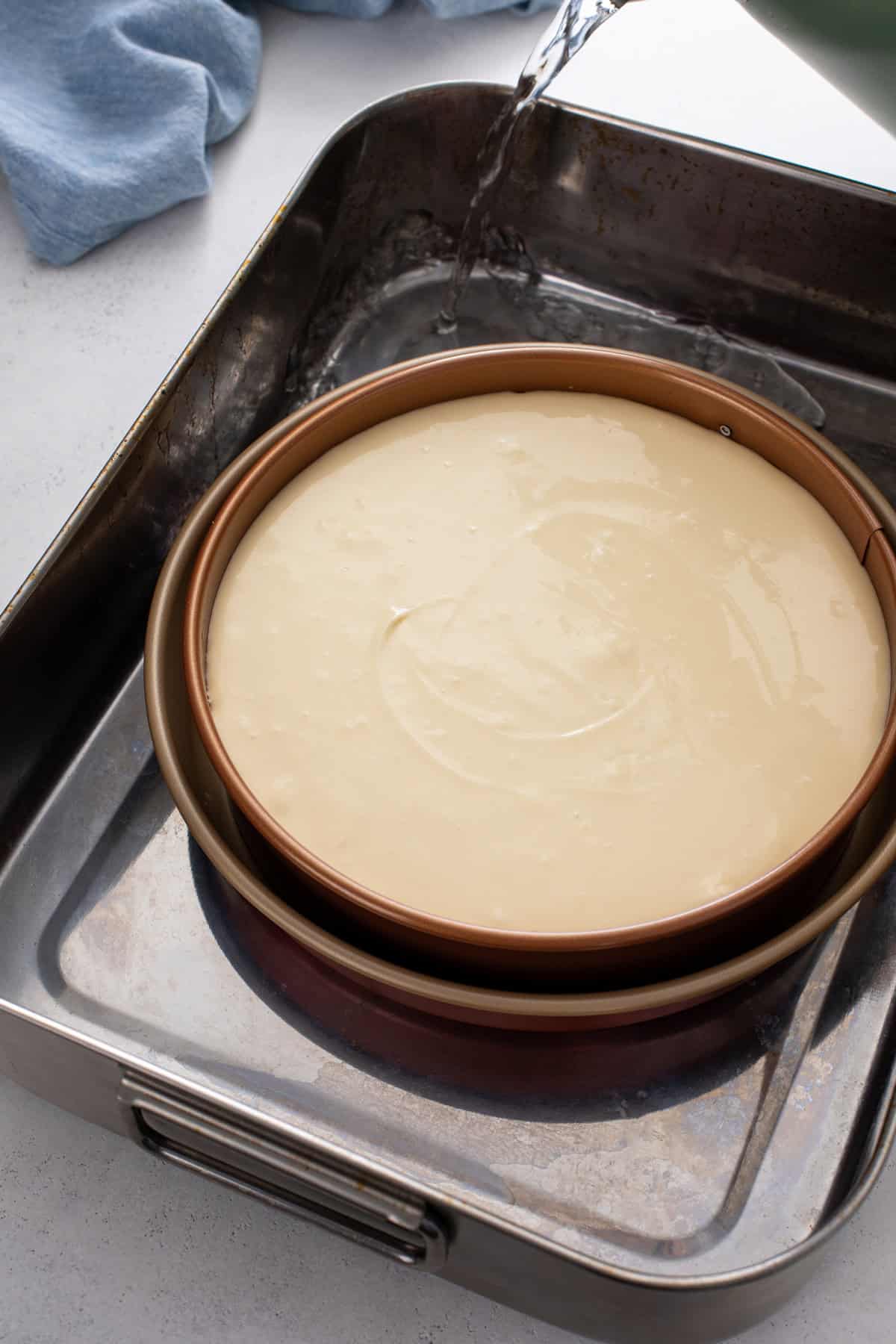 Hot water being poured into a water bath for baking a s'mores cheesecake.