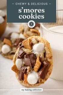 S'mores cookie leaning against a glass of milk on a countertop. Text overlay includes recipe name.