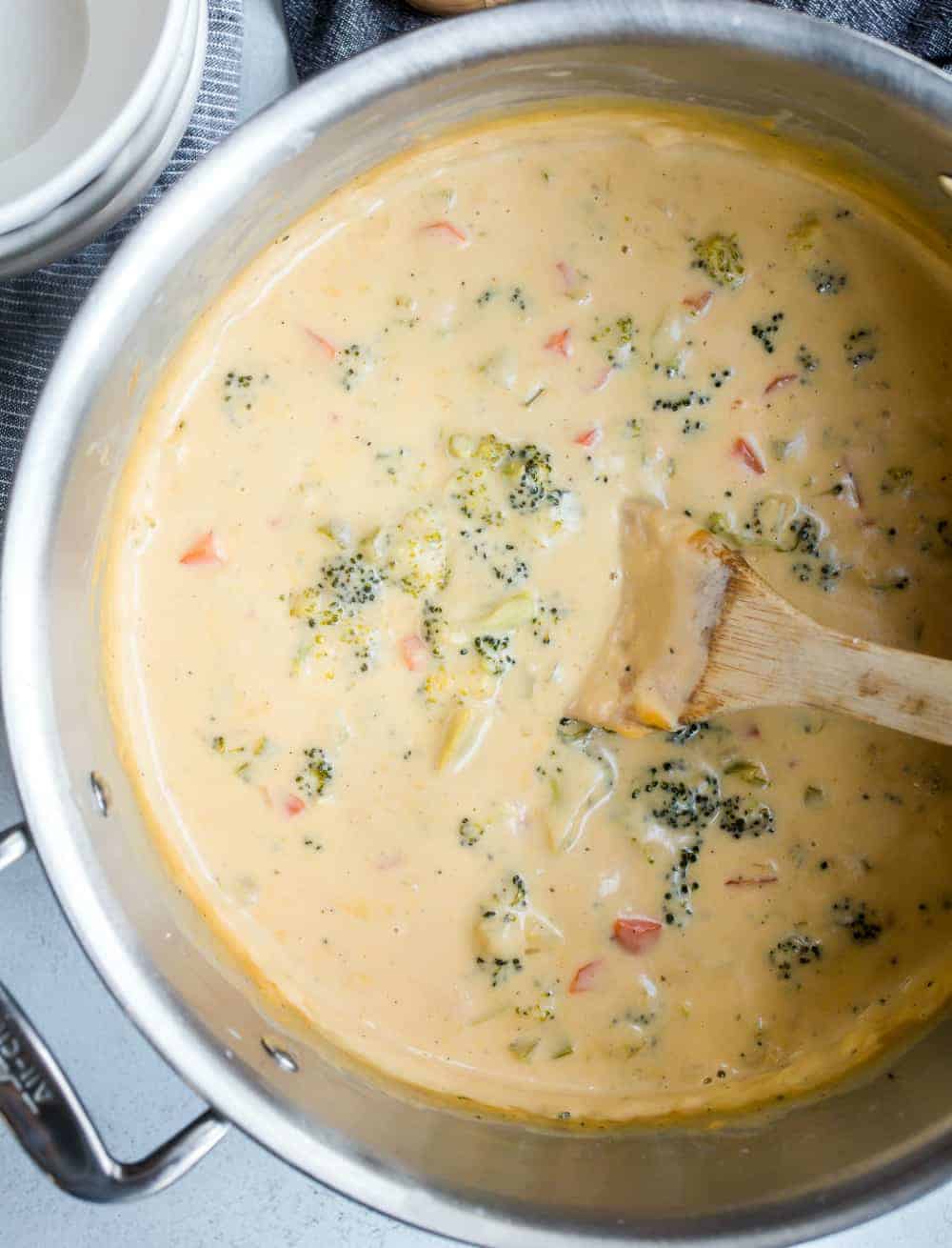 Wooden spoon stirring a pot of broccoli cheese soup