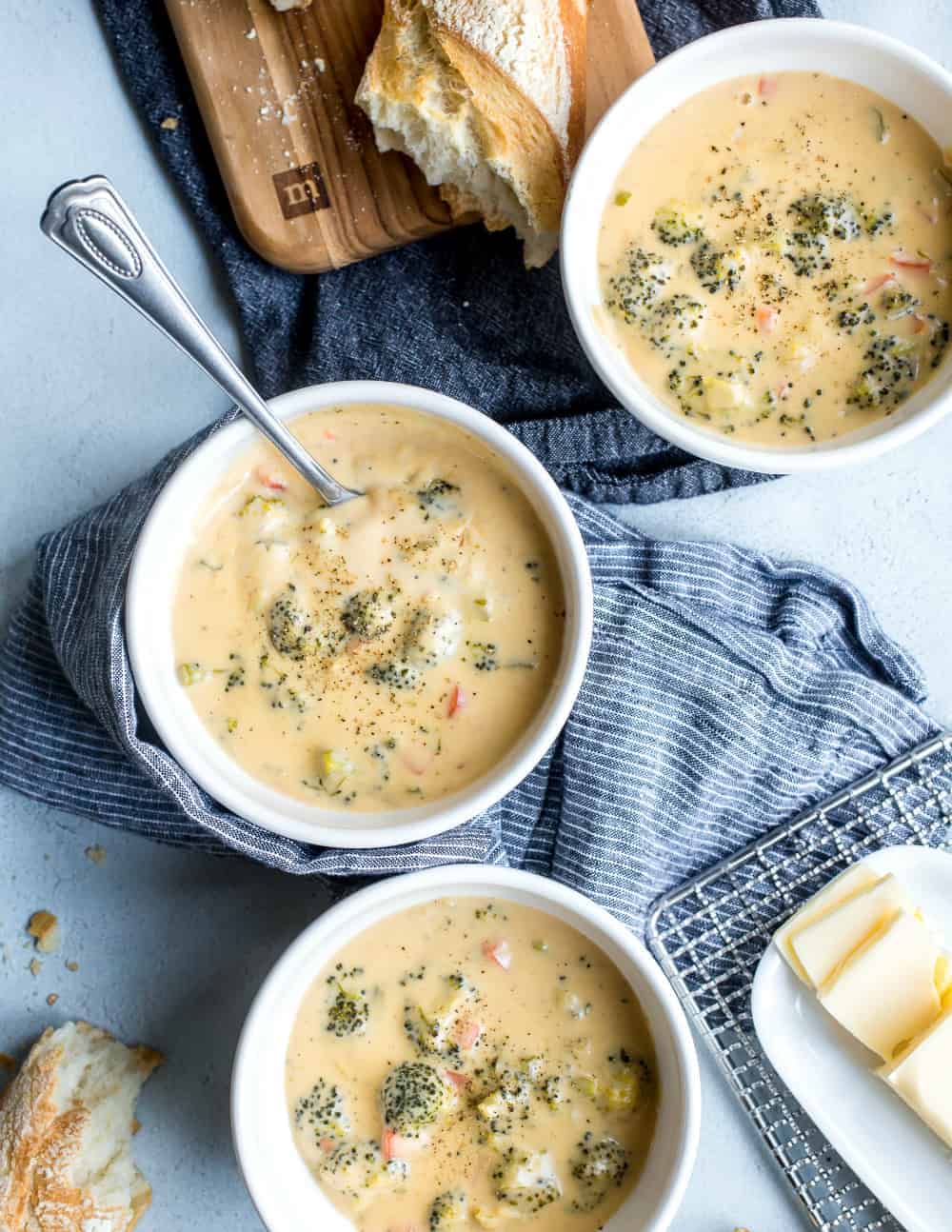 Bowls of broccoli cheese soup arranged next to bread and butter