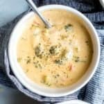 Overhead shot of broccoli cheese soup in a white bowl on a blue tea towel