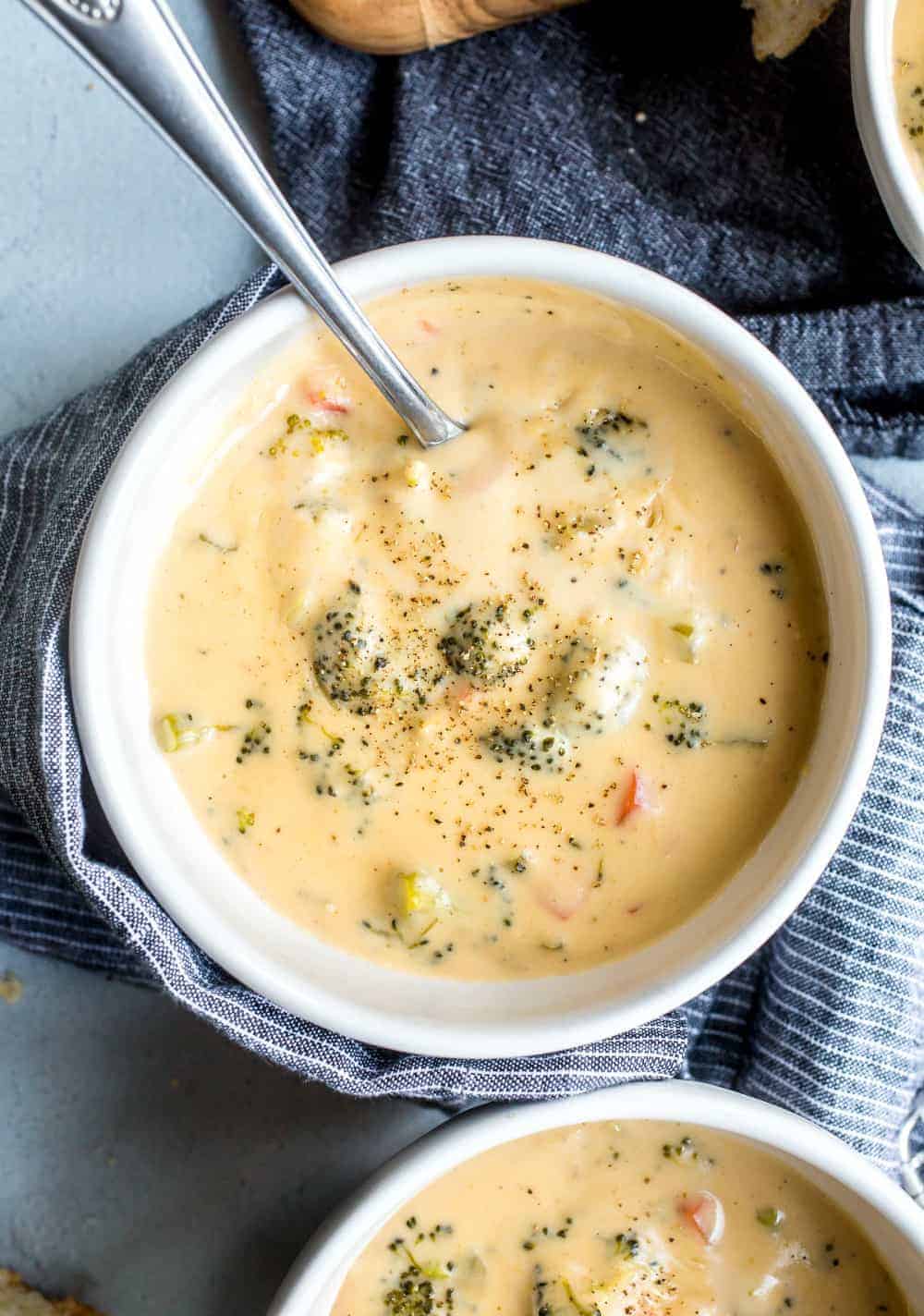 Overhead shot of broccoli cheese soup in a white bowl on a blue tea towel