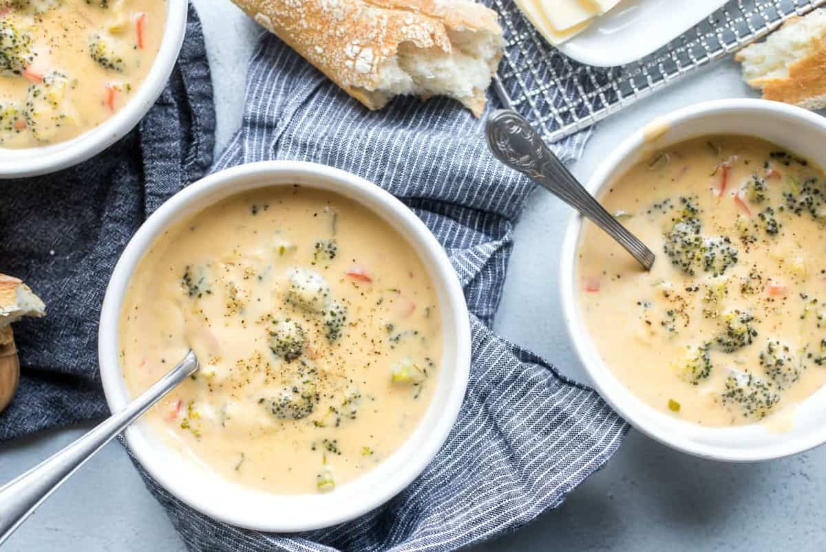 Overhead shot of bowls of broccoli cheese soup next to crusty bread