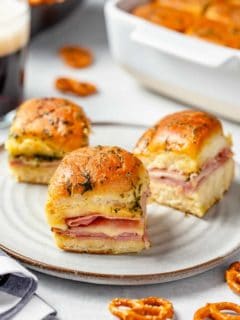 3 ham and cheese sliders on a white plate with a baking dish in the background