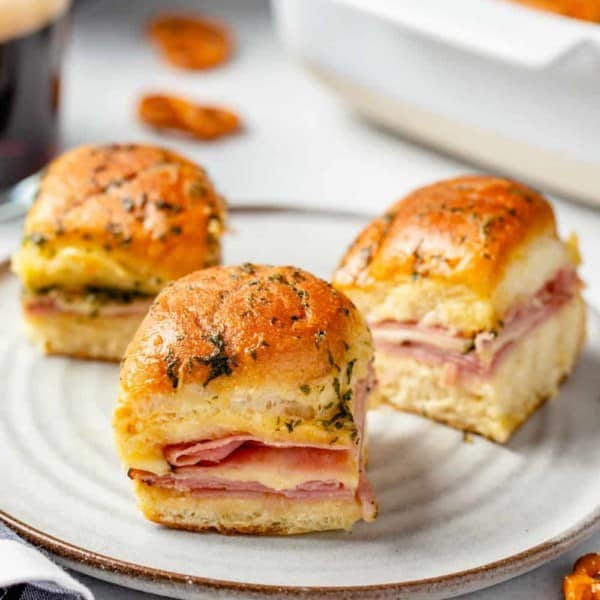 3 ham and cheese sliders on a white plate with a baking dish in the background