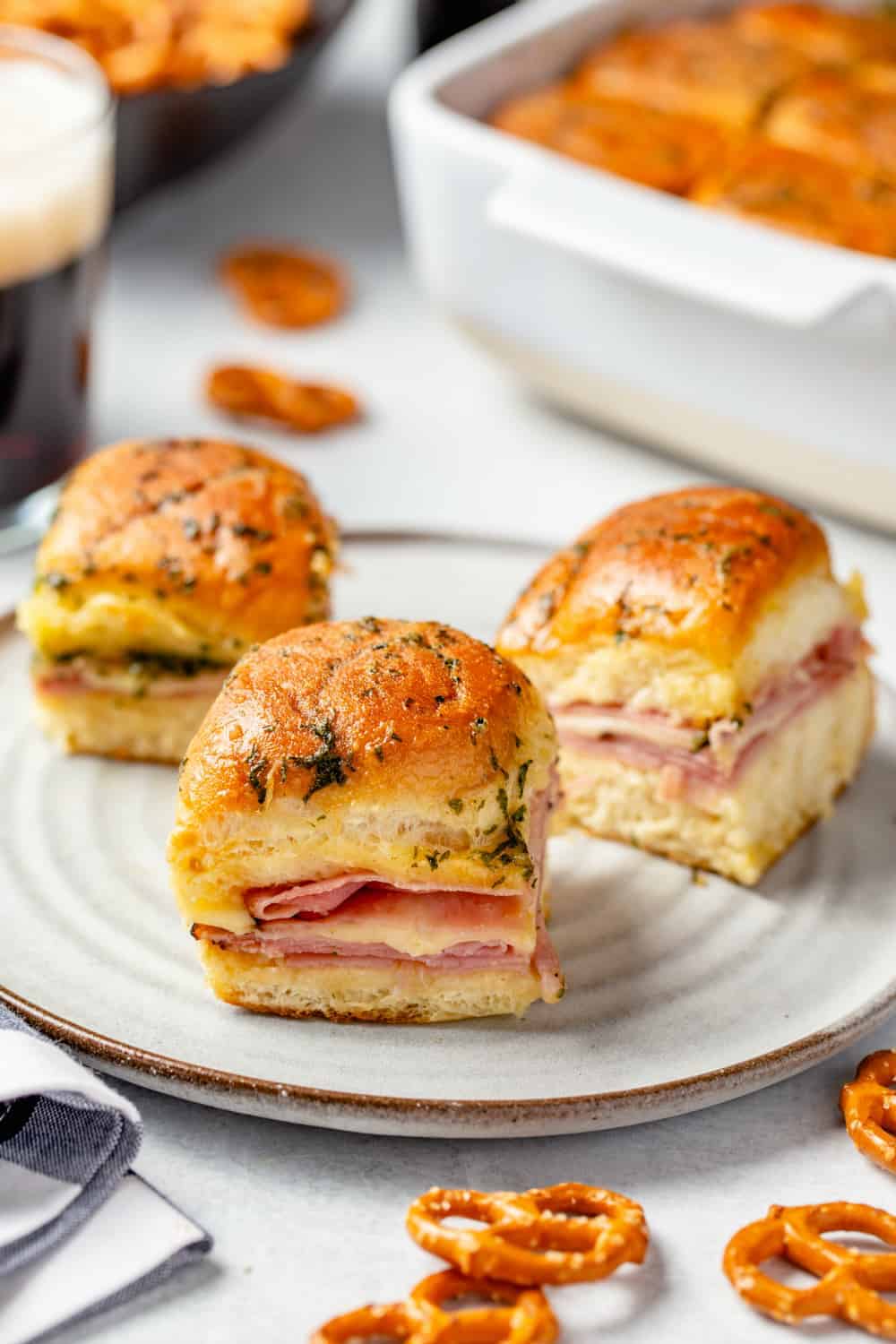 3 ham and cheese sliders on a white plate with a baking dish in the background