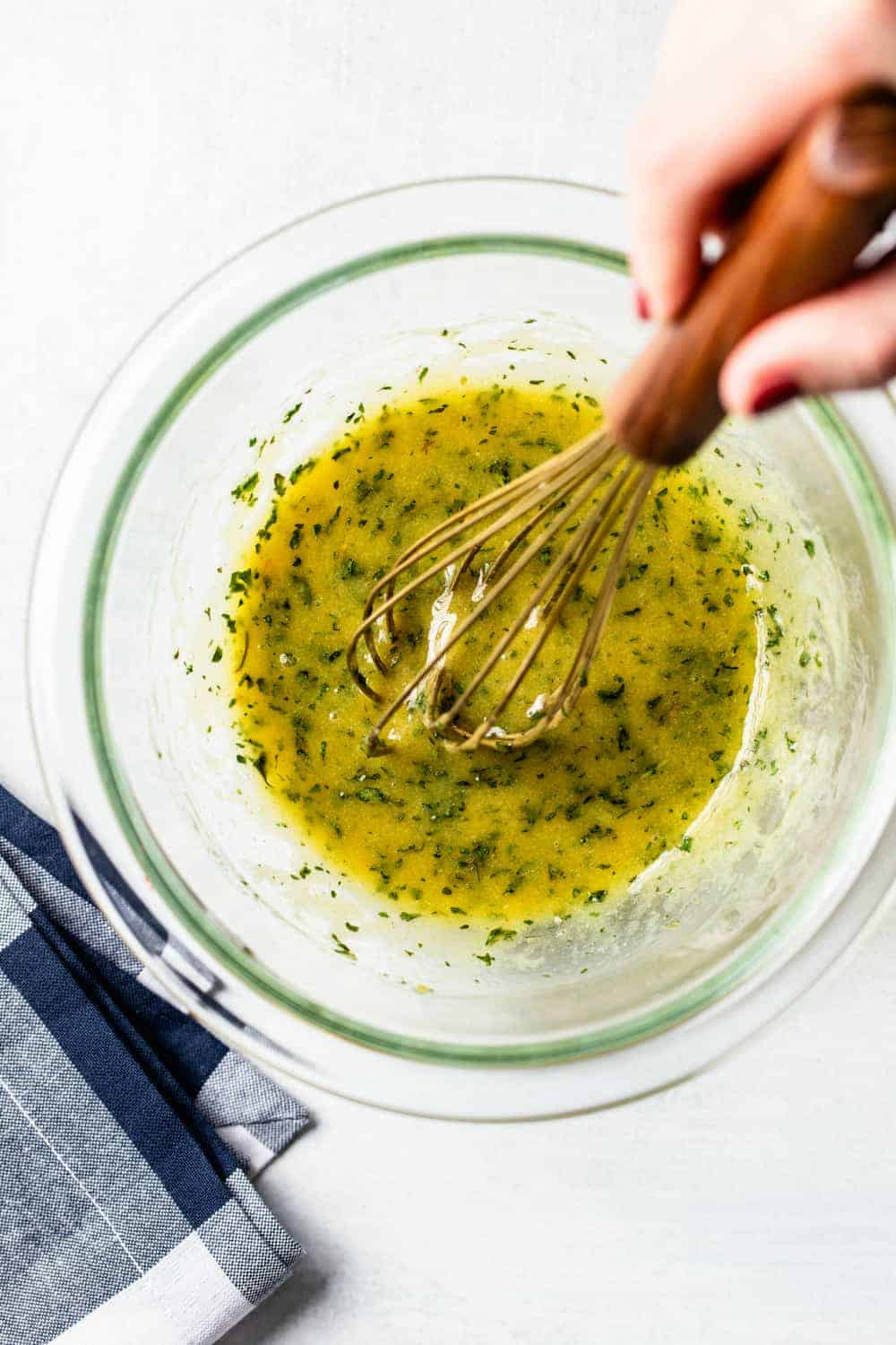 Hand whisking melted butter and herbs together in a small glass bowl