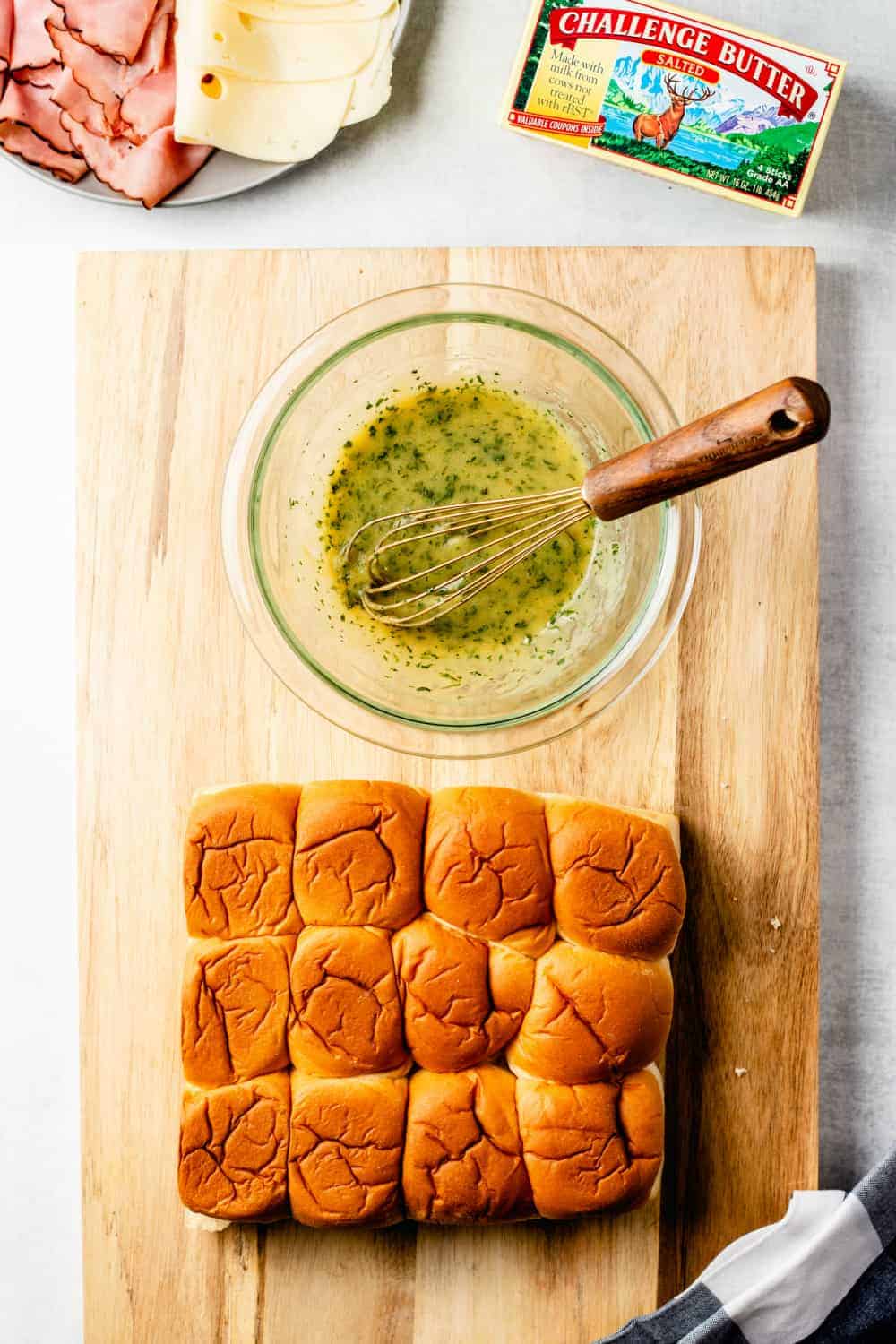 Hawaiian rolls and a bowl of melted butter mixed with herbs on a wooden cutting board