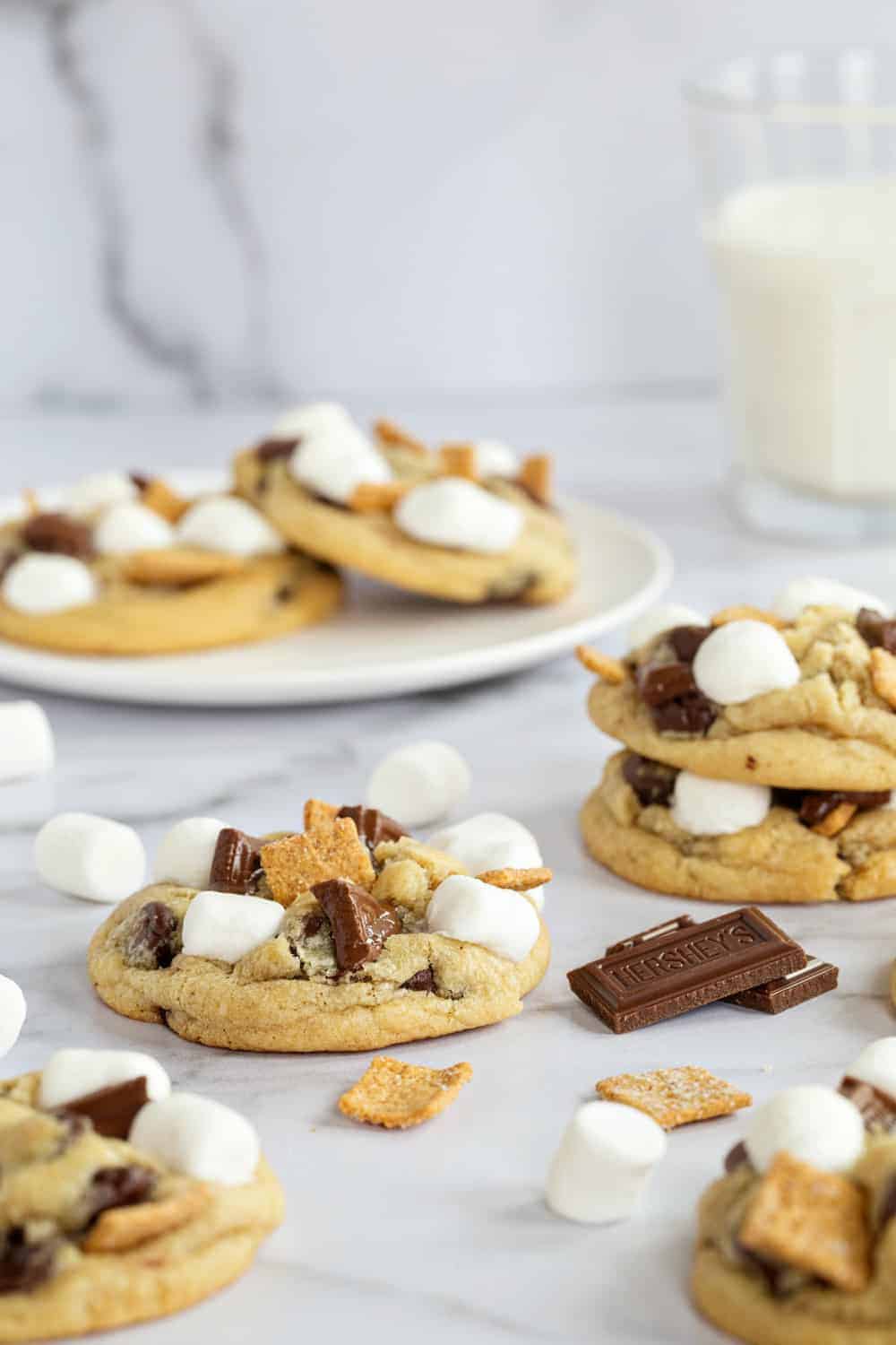 Plate of s'mores cookies in the background with more cookies in the foreground on a marble surface