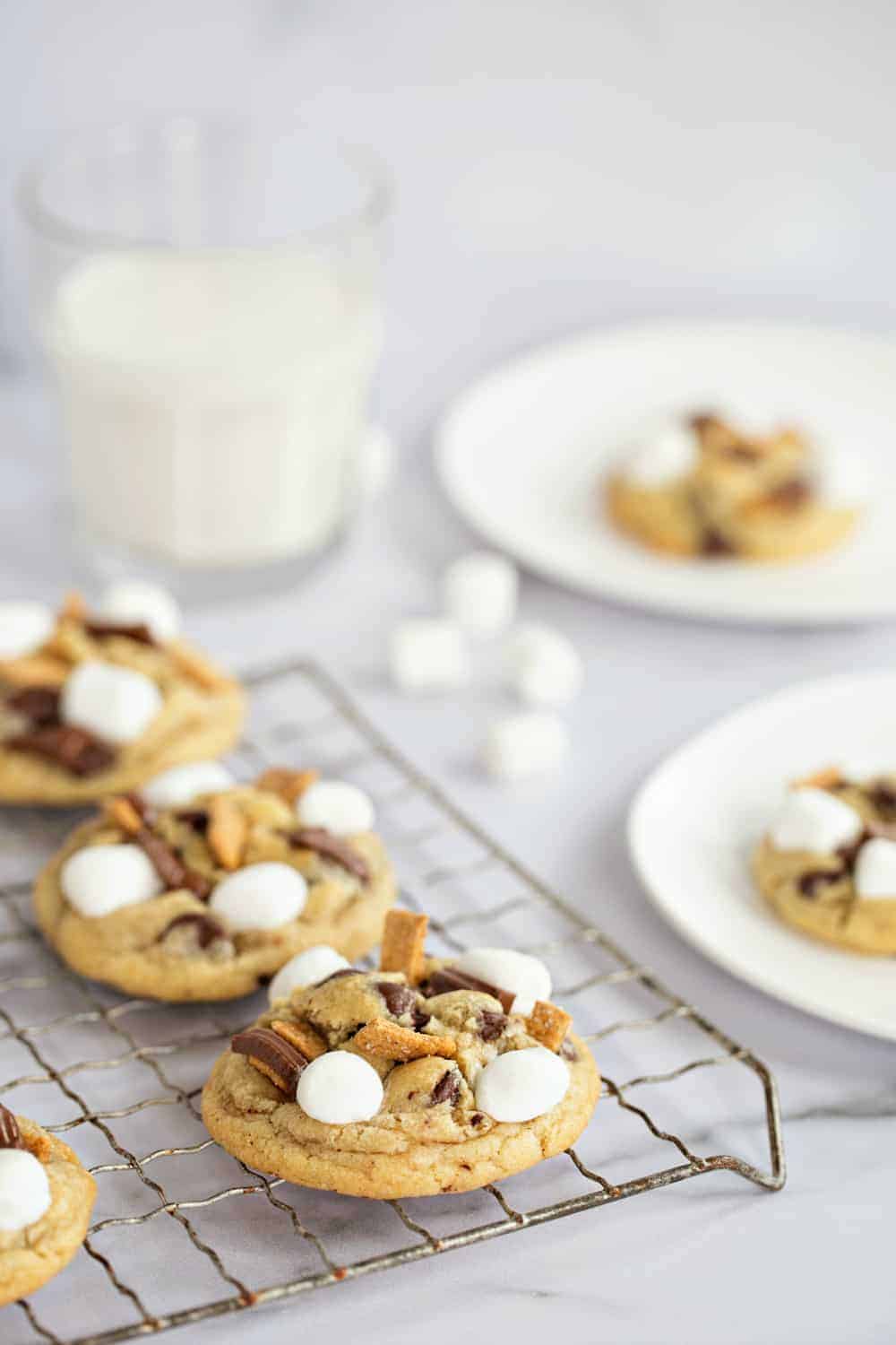 S'more's cookies on a metal cooling rack with white plates with cookies on them in the background