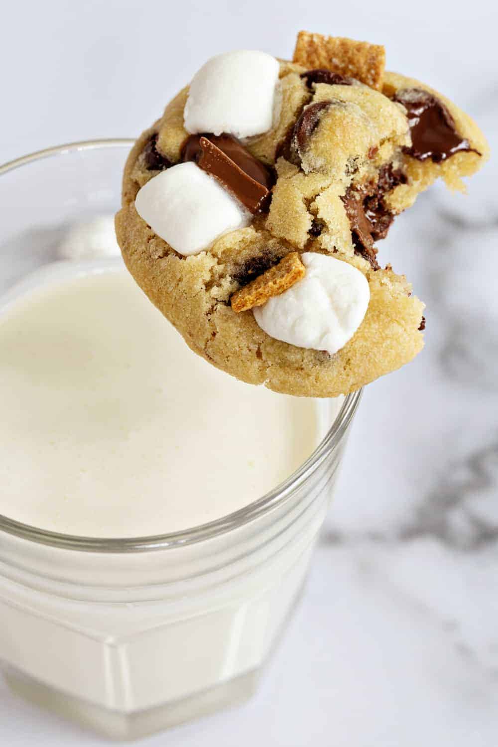 S'mores cookie with a bite taken out of it perched on the edge of a glass of milk