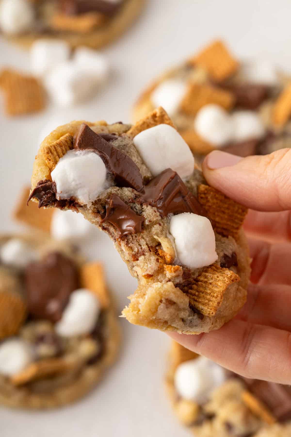 Hand holding up a s'mores cookie with a bite taken from it.