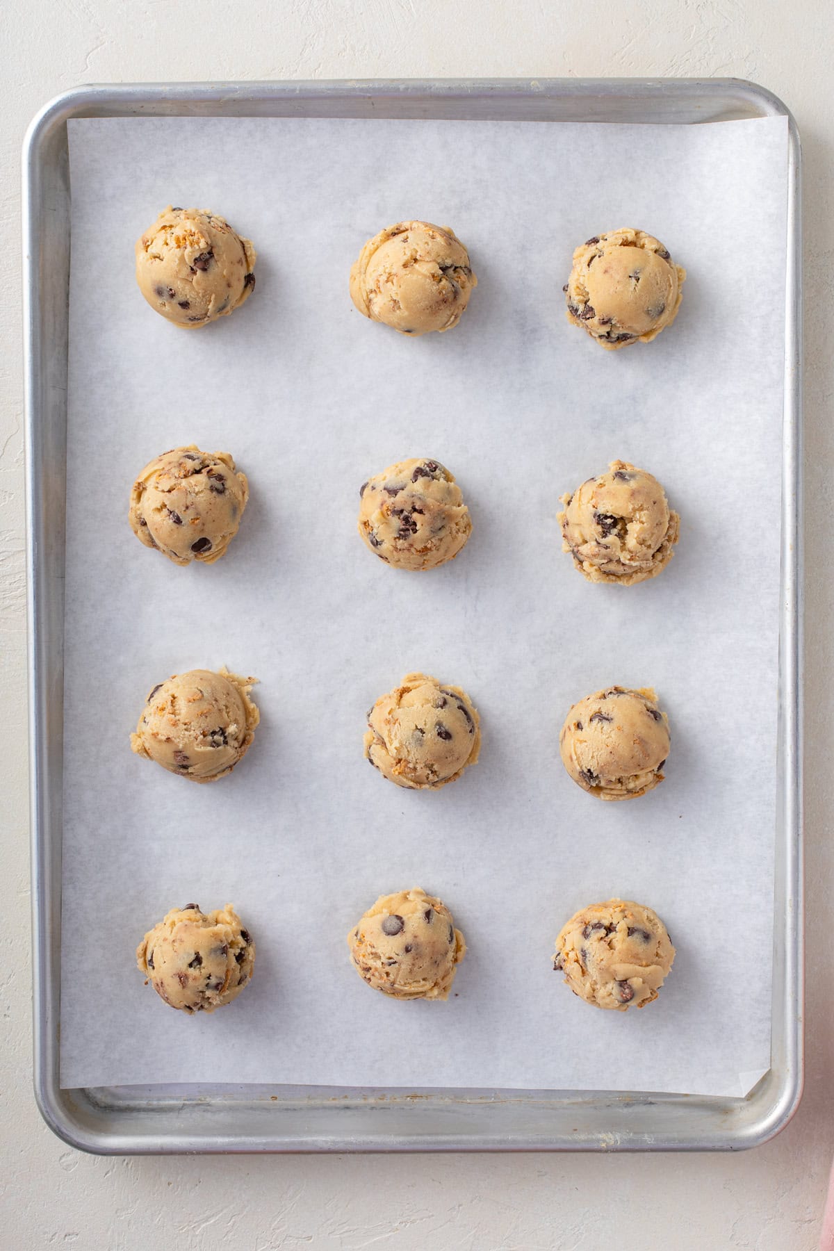 Balls of s'mores cookie dough portioned onto a parchment-lined baking sheet.