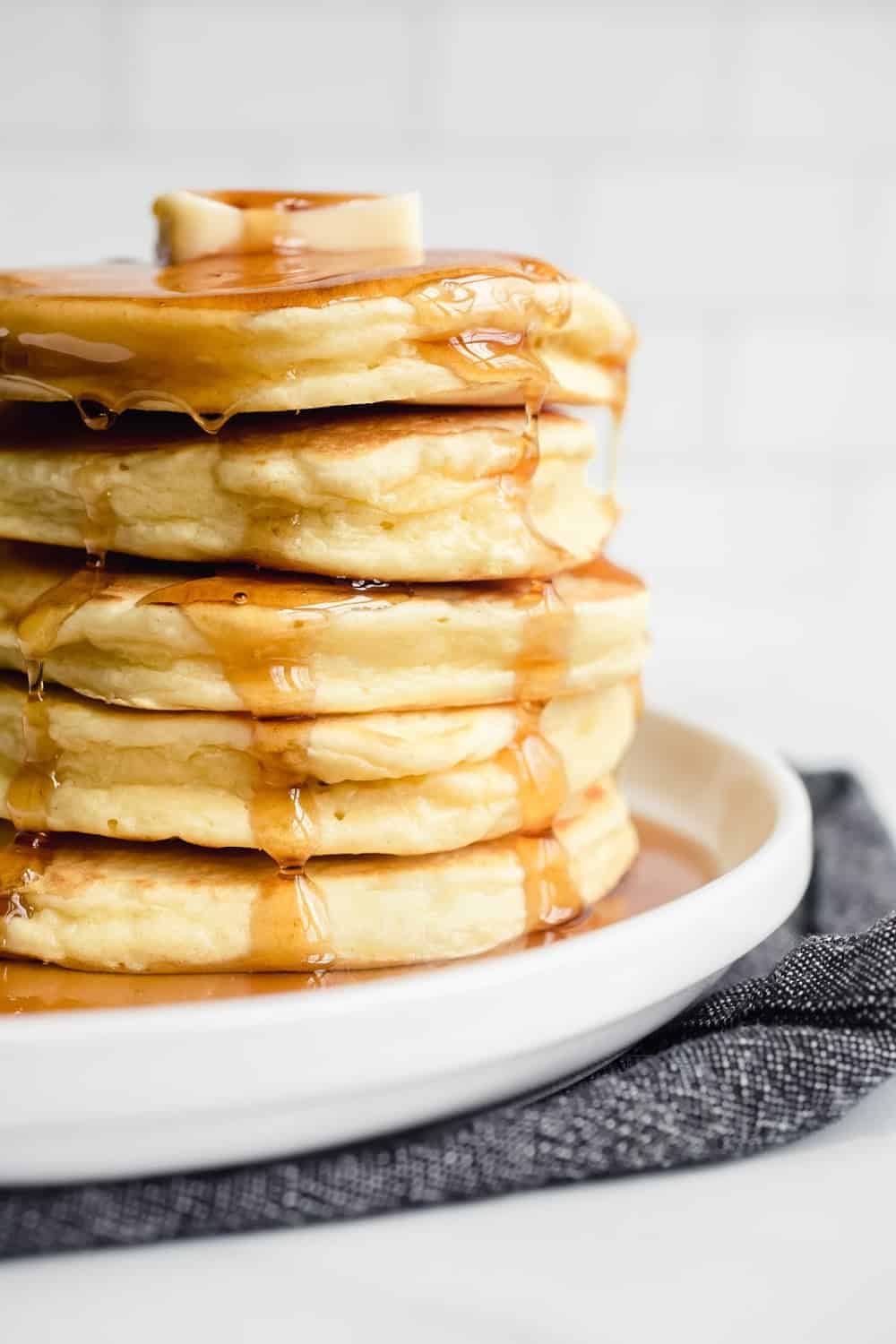 Stack of fluffy Bisquick pancakes on a white plate, topped with butter and syrup