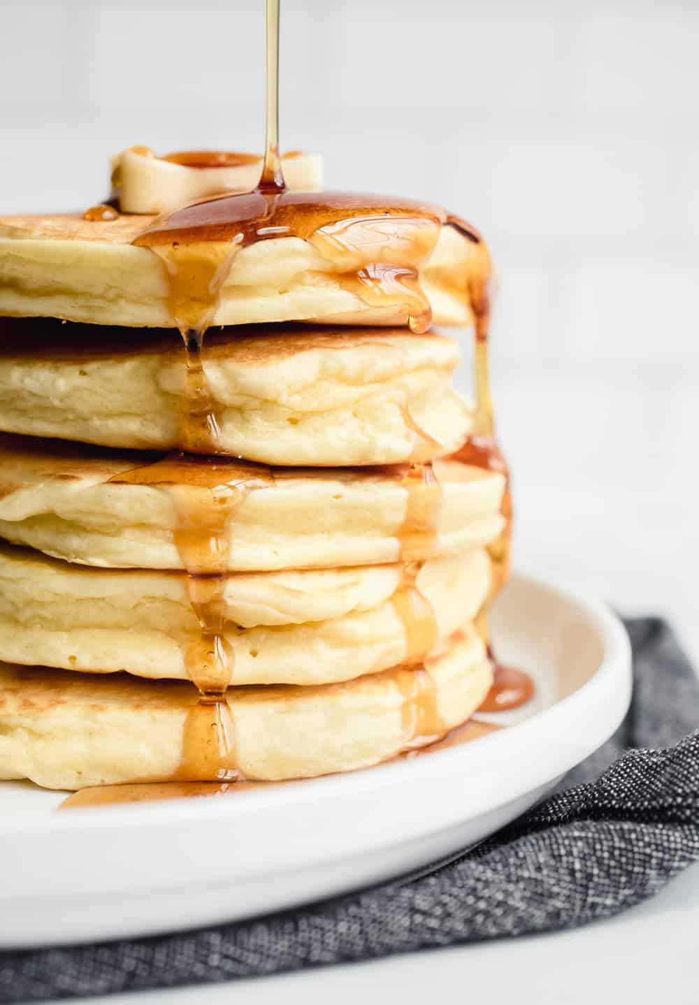 Syrup being drizzled over a stack of fluffy Bisquick pancakes on a white plate