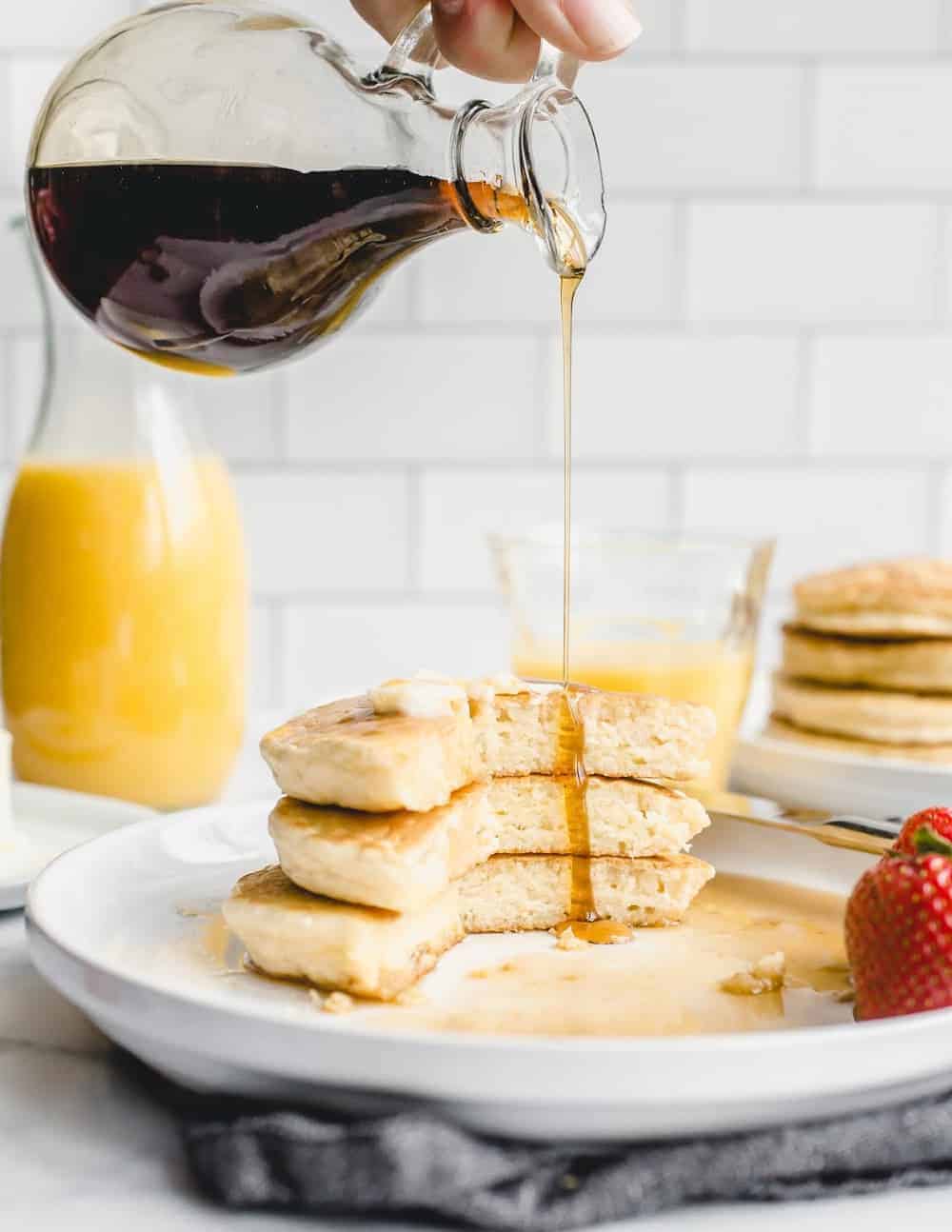 Small pitcher of syrup being poured over a white plate of Bisquick pancakes