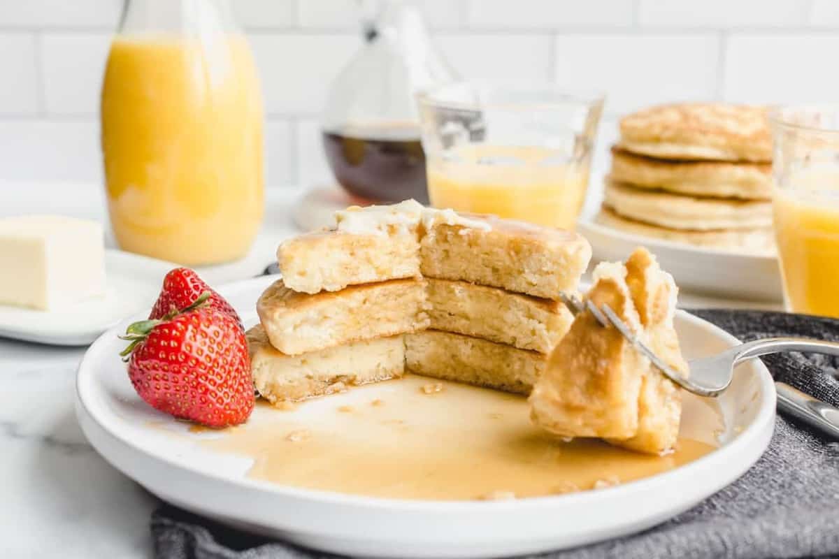 Stack of 3 Bisquick pancakes on a white plate, with a fork taking a bite out of the pancakes.