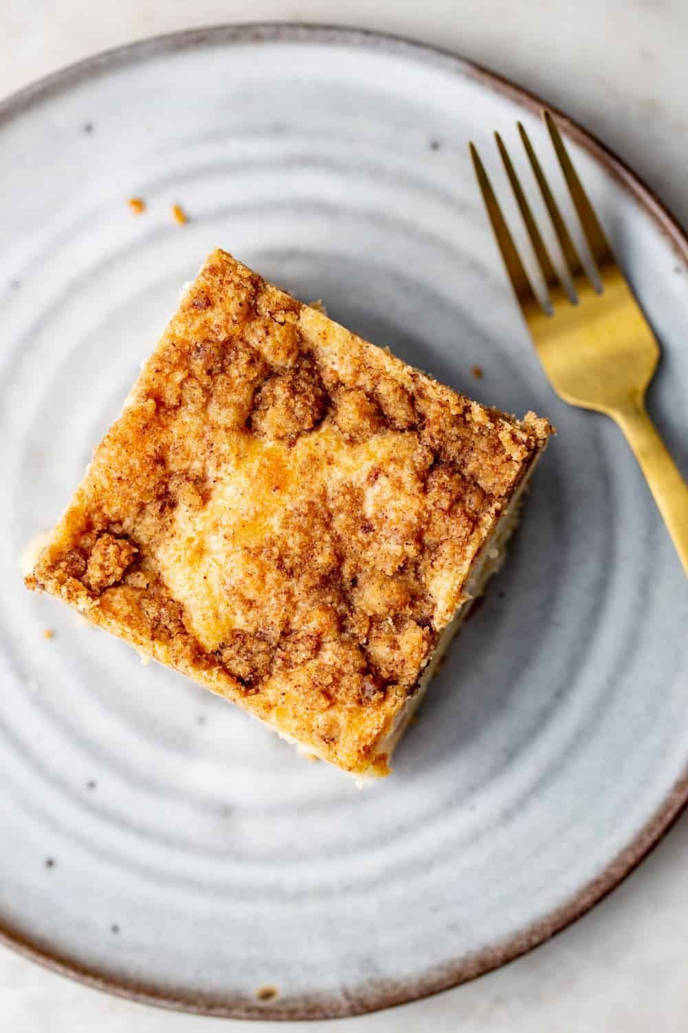 Overhead view of cinnamon coffee cake topped with cinnamon streusel on a white plate next to a gold fork