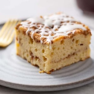 Close up side view of a slice of cinnamon coffee cake on a white plate. Cake topped with vanilla glaze and showing cinnamon streusel in the center
