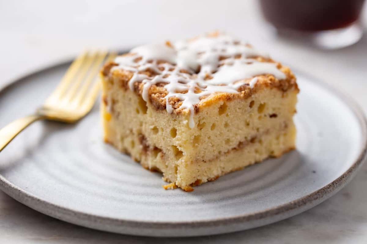 Close up side view of a slice of cinnamon coffee cake on a white plate. Cake topped with vanilla glaze and showing cinnamon streusel in the center