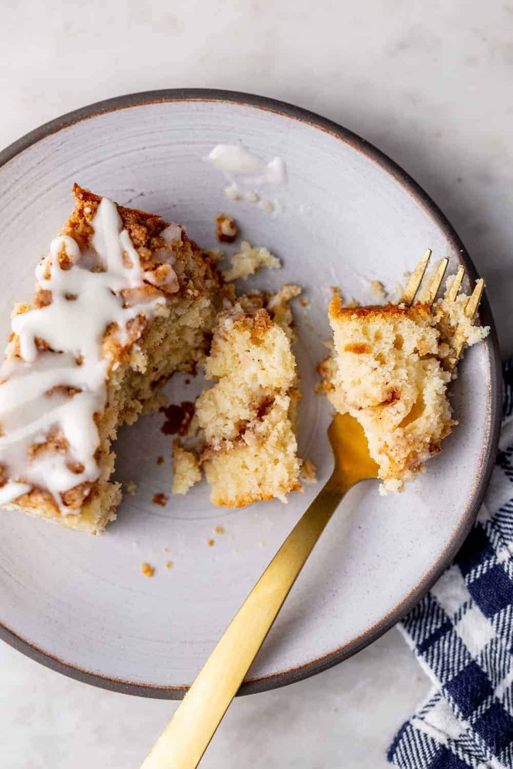 Gold fork cutting into a slice of cinnamon coffee cake on a white plate