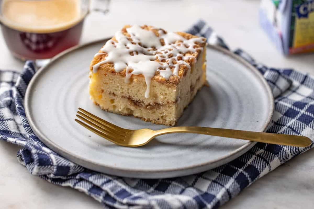 Angled view of a slice of cinnamon coffee cake on a white plate next to a gold fork, showing a line of cinnamon streusel in the middle of the cake