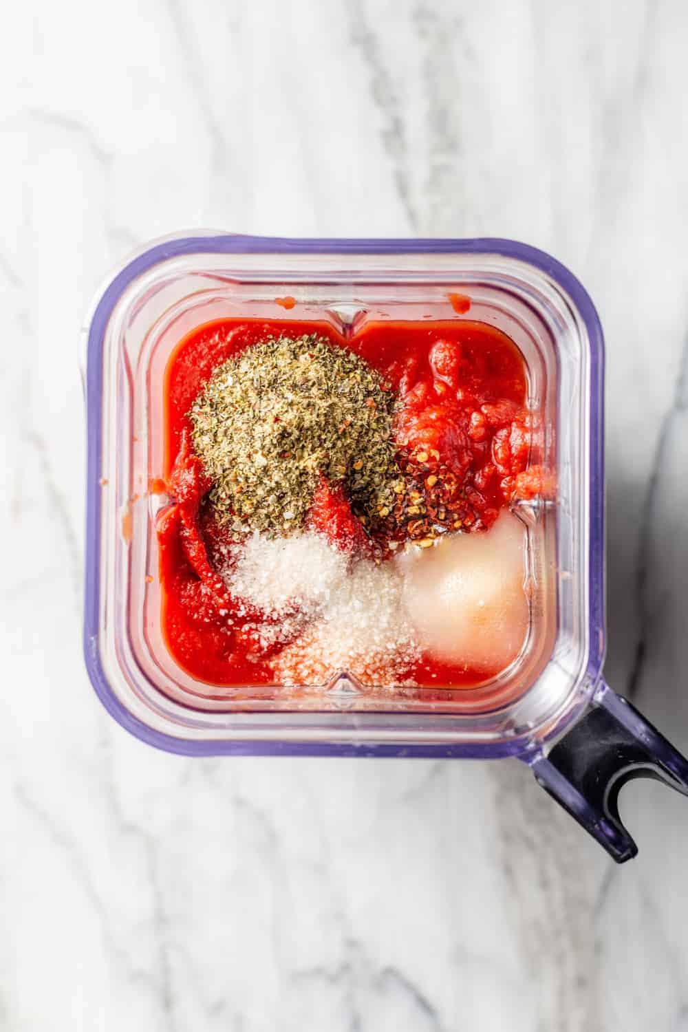 Overhead view of ingredients for tomato sauce in a blender on a marble surface