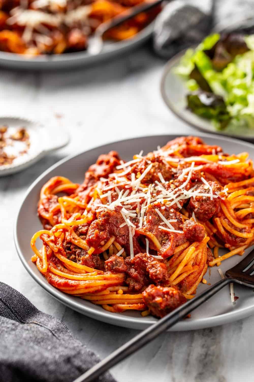 Side view of spaghetti and homemade meat sauce on a gray plate with a green salad in the background