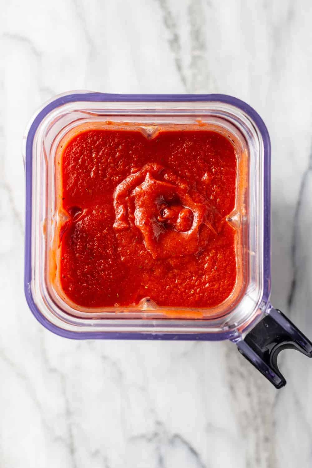 Overhead view of tomato sauce in a blender on a marble surface