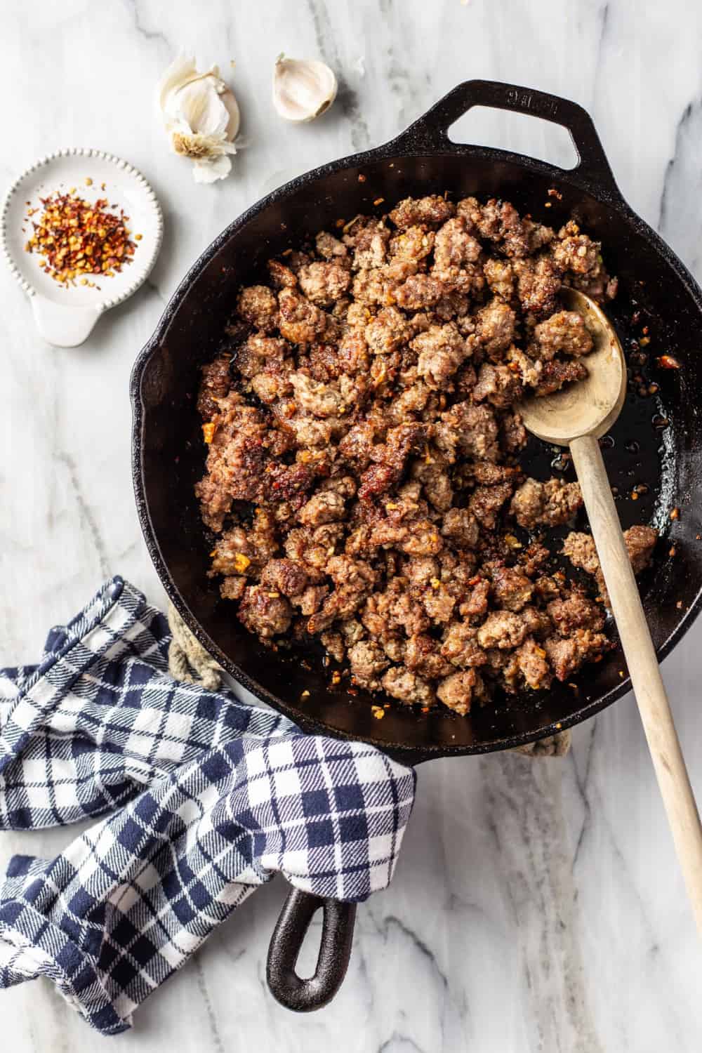 Cooked ground beef and sausage for homemade meat sauce in a black skillet on a marble surface