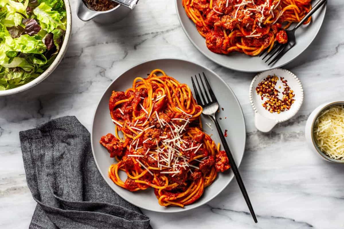 Plated spaghetti and meat sauce with a fork on the plate next to a green salad