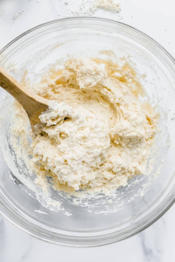 Wooden spoon stirring biscuit dough in a glass mixing bowl