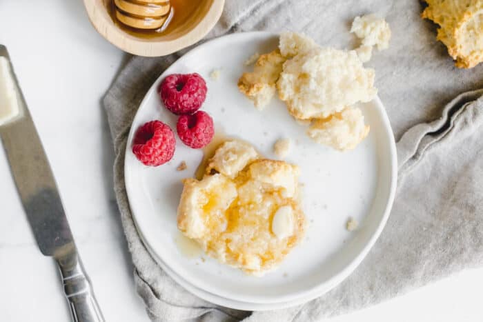 Overhead view of Bisquick biscuit on a white plate, topped with honey and butter. Plate is set on a gray napkin.