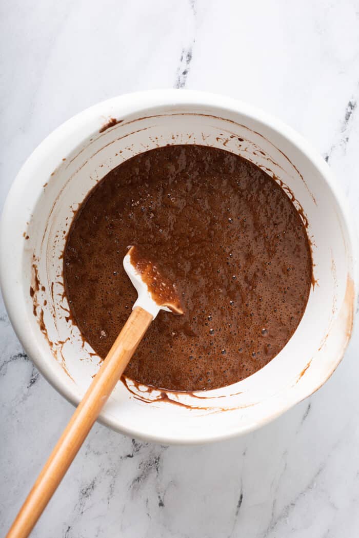 Batter for Hershey's Chocolate Cake in a white mixing bowl on a marble counter, being stirred by a white spatula